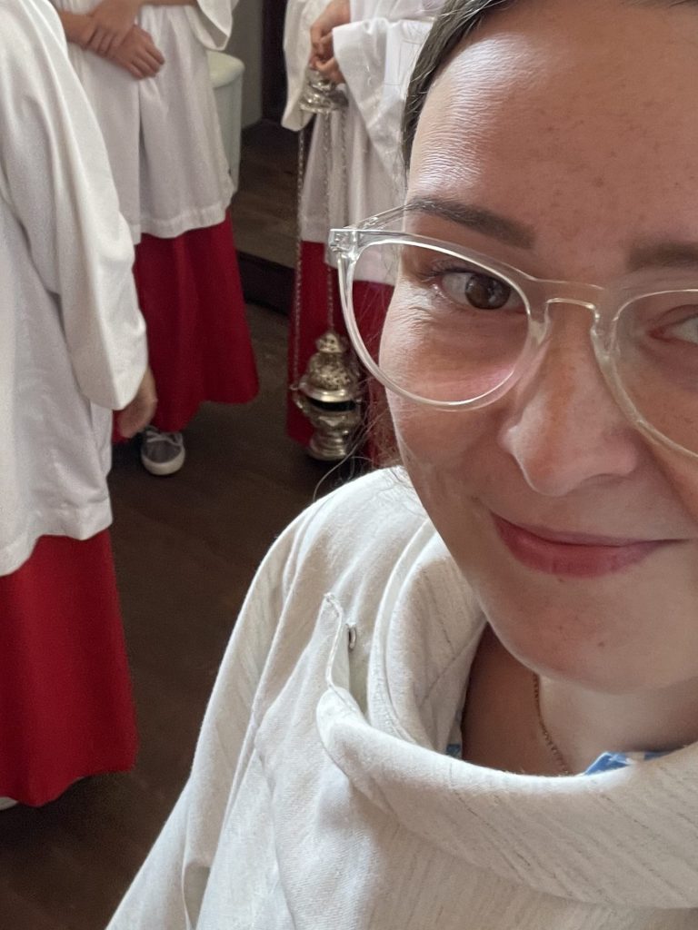 Sophie steht in einer Sakristei. Im Hintergrund sind Ministrant:innen zu stehen.